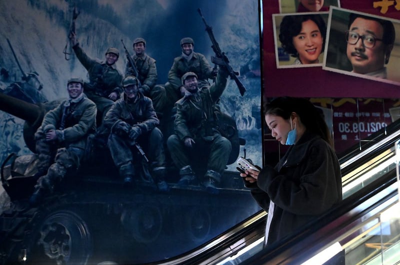 A woman rides at an escalator past a movie promotion poster for "The Battle of Lake Changjin," a blockbuster film on the Koren War, at a mall in Beijing, Oct. 11, 2021. Credit: AFP