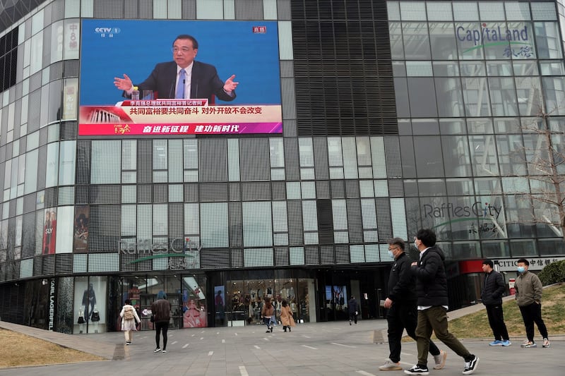 People walk past a giant screen showing a news conference by Chinese Premier Li Keqiang, following the closing session of the National People's Congress (NPC) at the Great Hall of the People in Beijing, March 11, 2022. Credit: Reuters