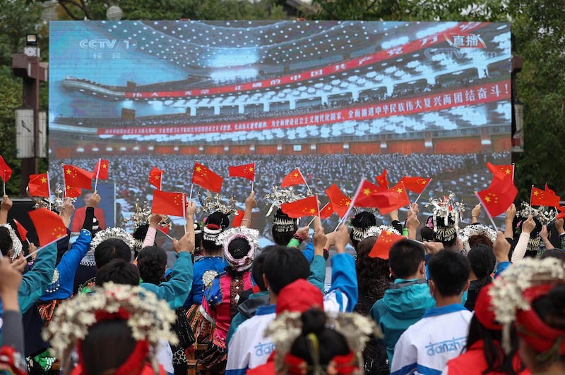 Ethnic minority members wave national flags as they watch the opening session of the 20th Chinese Communist Party Congress on a screen in Danzhai, in Chinaís southwestern Guizhou province, Oct. 16, 2022. Credit: AFP