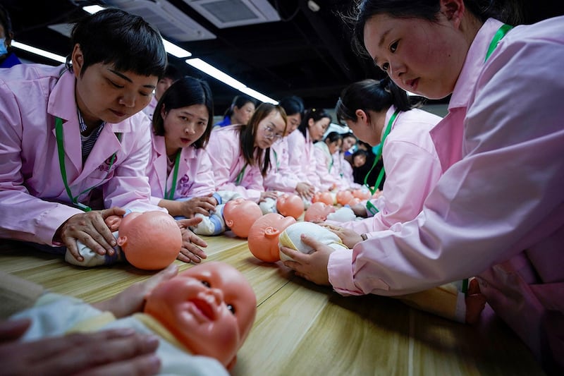 Women train with plastic baby dolls as they take part in a nursing skills class at Yipeitong training center in Shanghai, March 2, 2023. (Aly Song/Reuters)