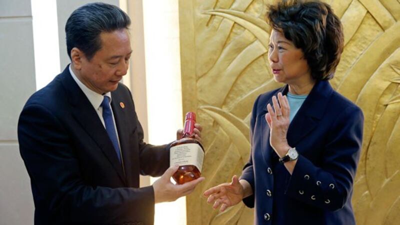 China's Transport Minister Li Xiaopeng (L) holds a bottle of whiskey given to him by US Secretary of Transportation Elaine Chao (R) after a signing ceremony at the Ministry of Transport in Beijing, April 27, 2018.