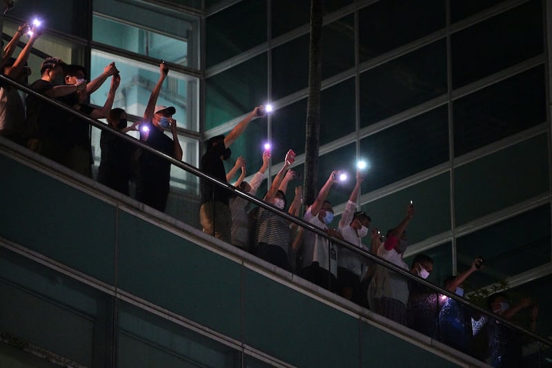 Employees of the Apple Daily newspaper shine phone torches from an office balcony and shout thanks to supporters down on the street below in Hong Kong, June 23, 2021. Credit: AFP