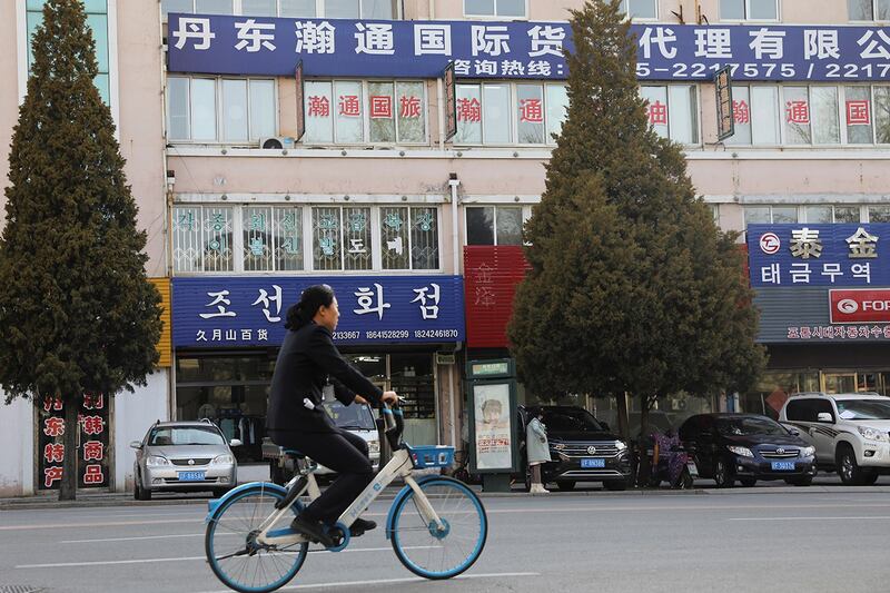 资料图：一名妇女骑着脚踏车经过紧邻朝鲜的辽宁省丹东市区，路旁的招牌显示一家与朝鲜贸易的公司。(路透社资料图片)