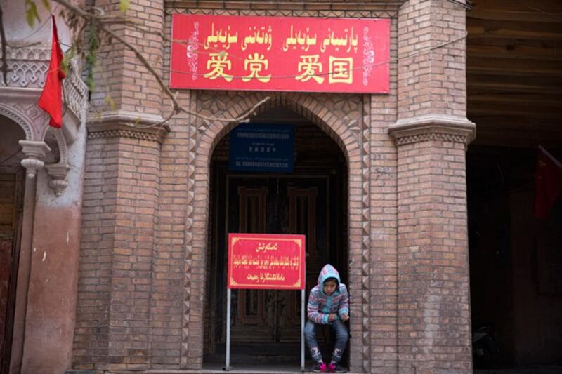 A child sits near the entrance to a mosque with a banner reading ‘Love the party, Love the country' in the old city district of Kashgar in northwestern China's Xinjiang region, Nov. 4, 2017. (Ng Han Guan/AP)