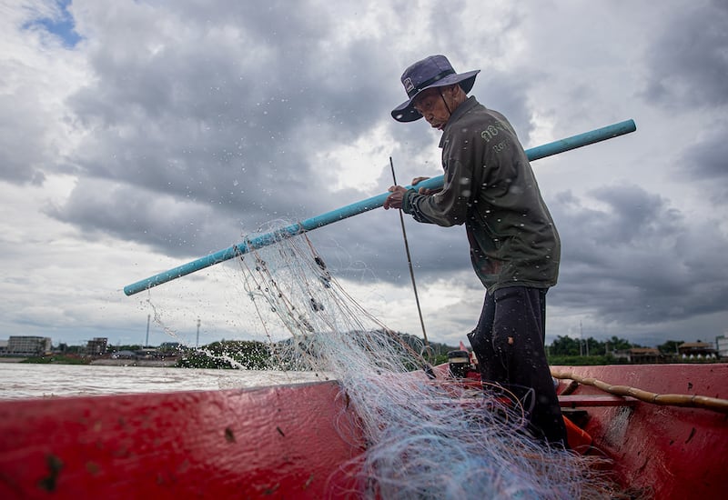 Stormclouds brew above fisherman Boonrat Chaikeaw as he casts his net into the Mekong River by Chiang Khong by the border between Thailand and Laos.