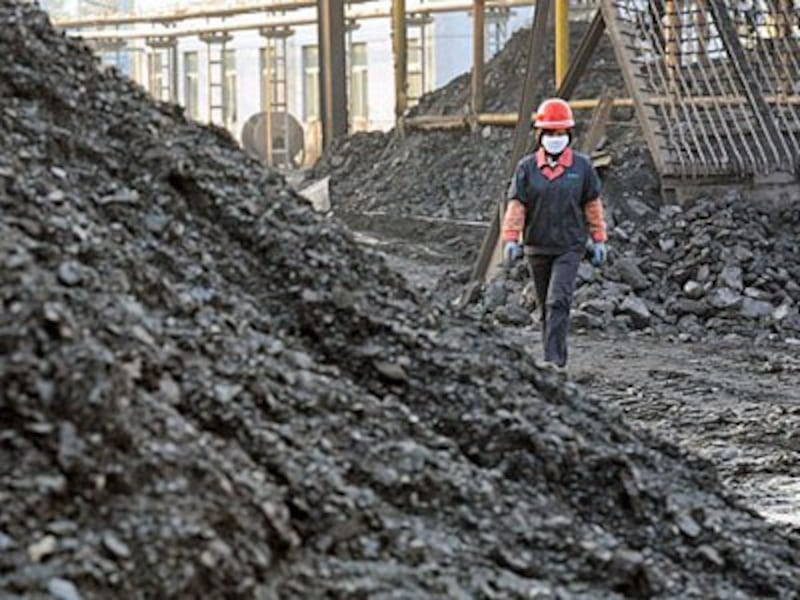 A Chinese worker walks past piles of coal in a coalyard at a mine in Huaibei, eastern China's Anhui province, Nov. 7, 2016.