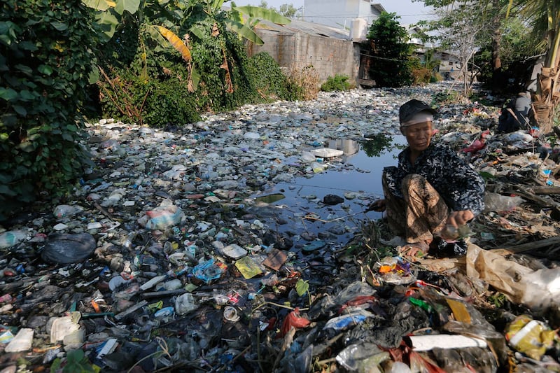 A scavenger collects plastic materials to be sold to recycling plants on the Bahagia river in Bekasi, Indonesia, Aug. 1, 2019.