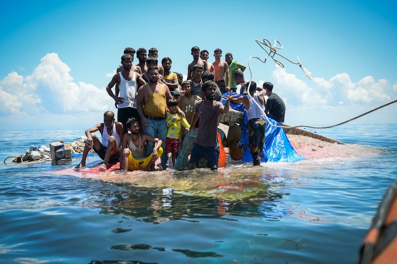 Ethnic Rohingya refugees stand on their capsized boat as rescuers throw a rope to them off West Aceh, Indonesia, on March 21, 2024.