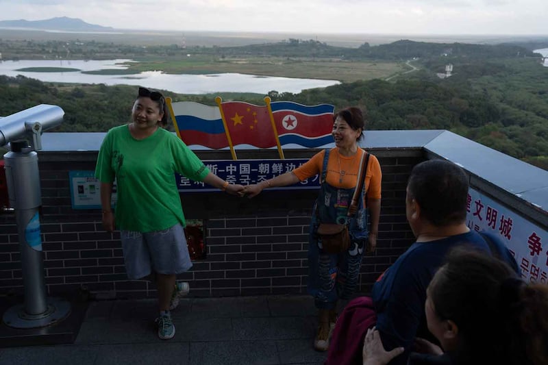 Visitors hold hands near the Russia, China and North Korean flags displayed at China's Yiyanwang Three Kingdoms viewing platform, which has a view of the three countries, Sept. 11, 2023. Credit: Ng Han Guan/AFP