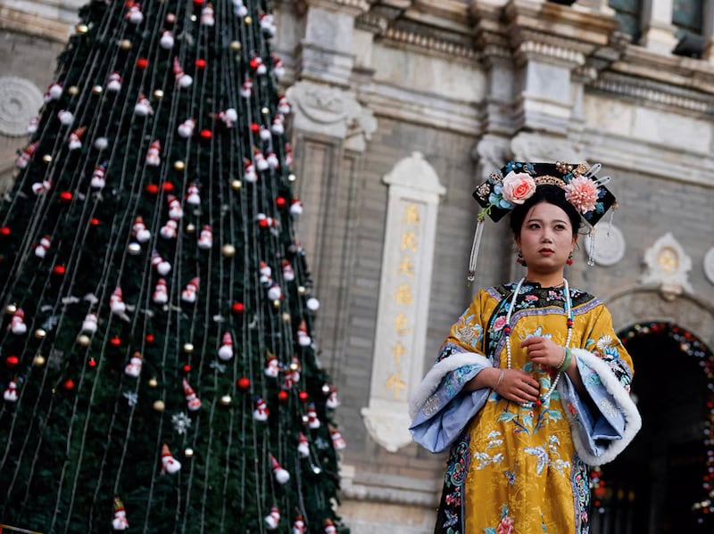 A woman wearing Manchu-style clothing poses in front of a Christmas tree at a church in Beijing, Dec. 20, 2024.