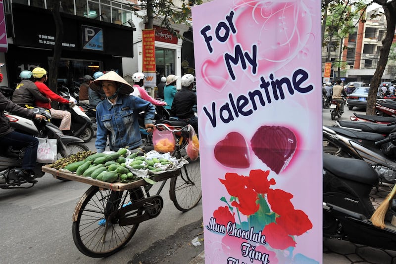 A woman stands selling fruits next to a shop offering Valentine's Day-related gifts on a street in Hanoi, Vietnam, Feb. 12, 2010.