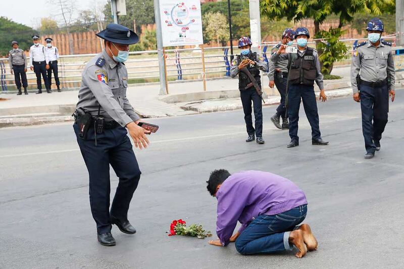 A protest supporter offers flowers and kneels on a road before a police officer in Mandalay in early February. (Associated Press)