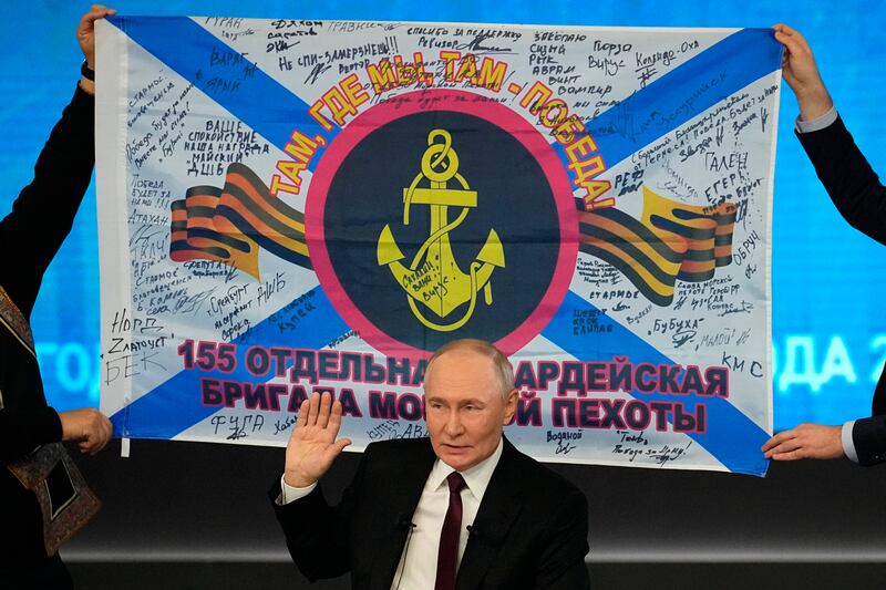 Russian President Vladimir Putin speaks during his annual news conference at Gostinny Dvor in Moscow, Russia, Thursday, Dec. 19, 2024, as men hold a replica of the banner of the 155th Marine Brigade of the Pacific Fleet, participating in a special military operation in Ukraine in the background.