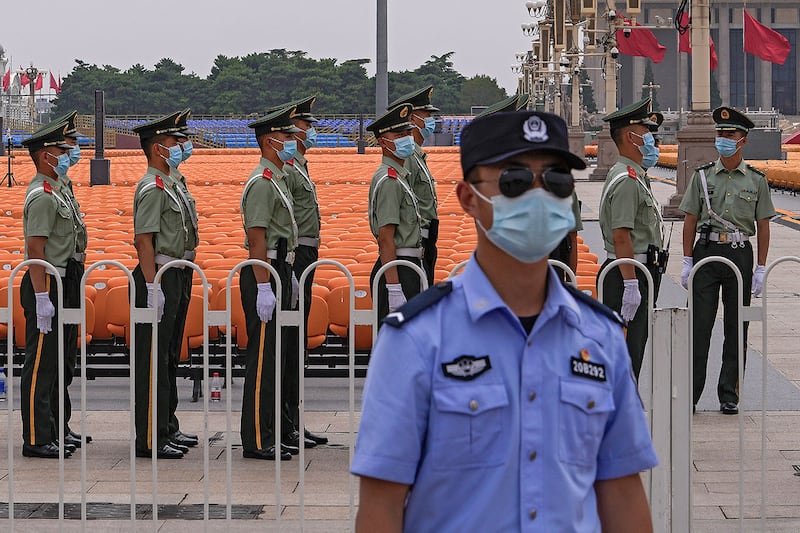 2021年6月28日，北京天安门广场上一排排座位旁，一名戴着口罩的警察在准备执勤的中国准军事人员旁边站岗。