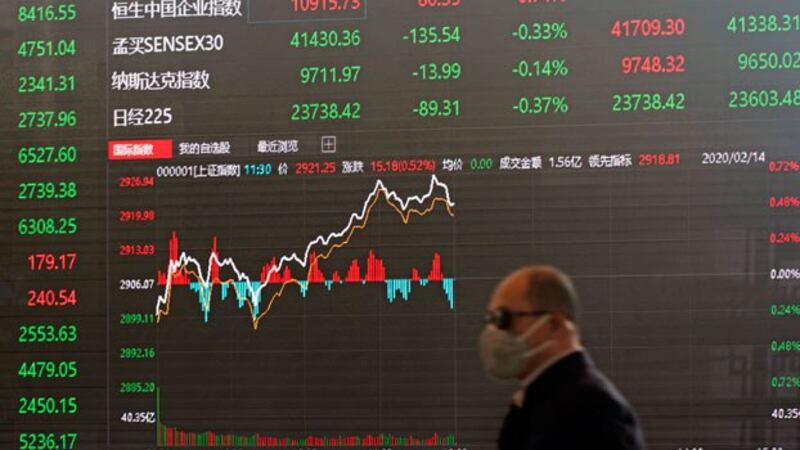 A man wearing a protective mask walks in front of an electronic display board in the lobby of the Shanghai Stock Exchange building in Shanghai, China, Feb. 14, 2020.