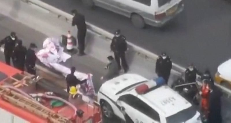 The protester [in orange] who hung the banners off a Beijing overpass on Oct. 13, 2022 is placed in a police car. Credit: Screenshot from Reuters video