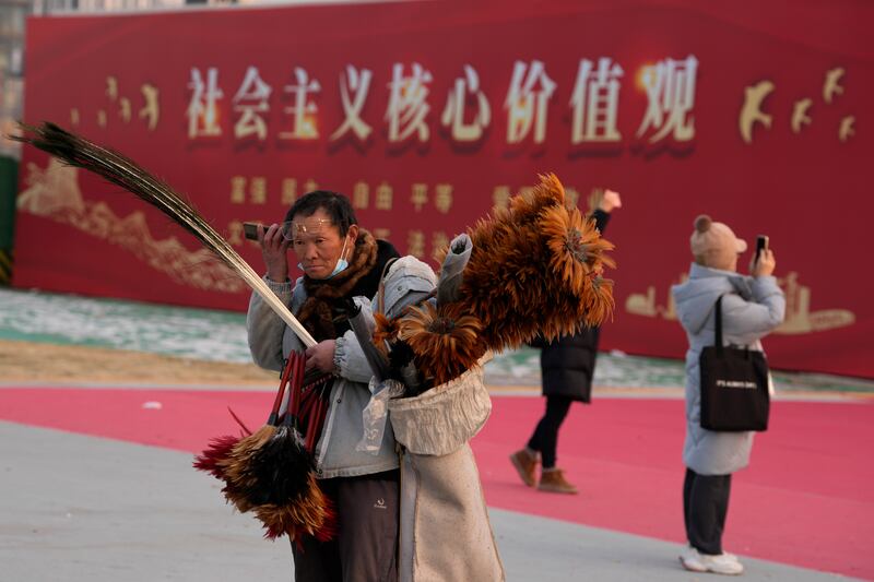 2024年1月20日，北京一名街头小贩在“社会主义核心价值观”宣传牌旁边一边听手机、一边兜售鸡毛掸子。