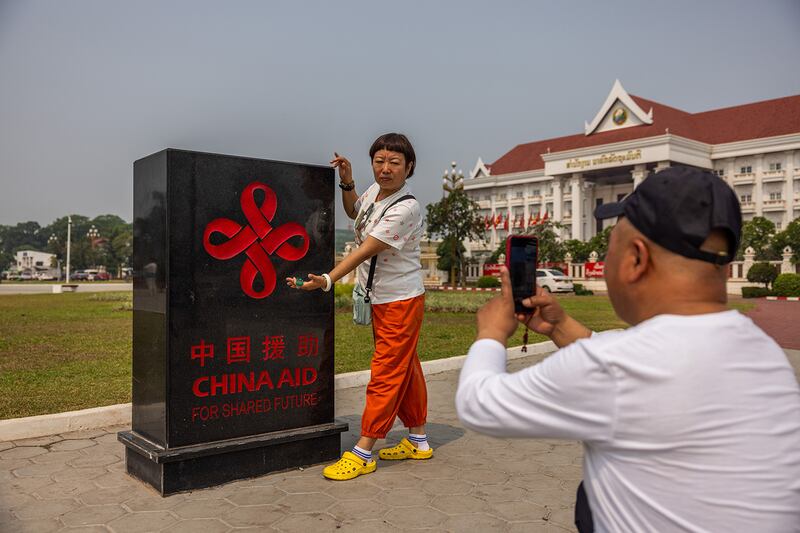 Chinese tourists take a photo with a China Aid plaque at the Patuxay Victory Monument on April 8, 2024, in Vientiane, Laos.