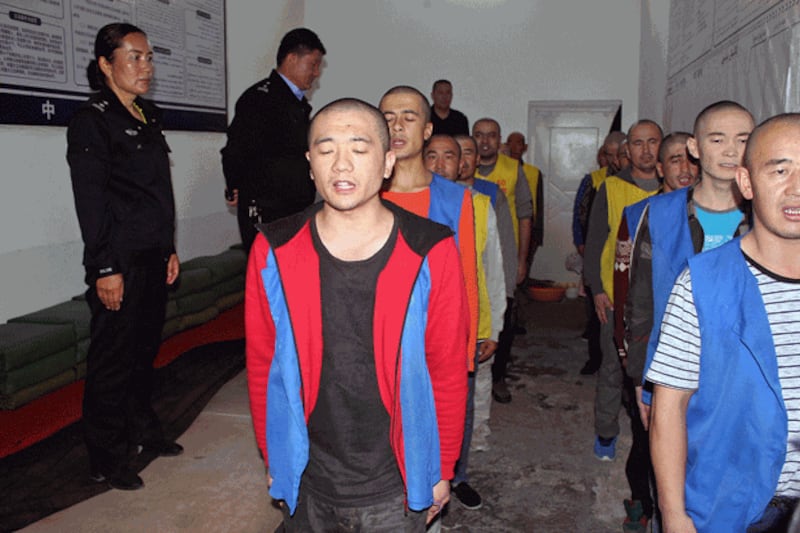 Police guard detainees as they stand in line apparently reciting or singing at the Tekes County Detention Center in northwestern China's Xinjiang region in an undated photo. Credit: AFP/The Victims of Communism Memorial Foundation