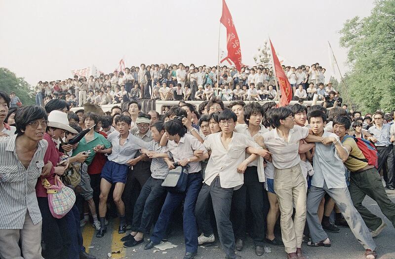 1989年6月3日，在北京人民大会堂附近，支持民主的抗议者手挽手阻止愤怒的人群追逐撤退的士兵。（美联社）