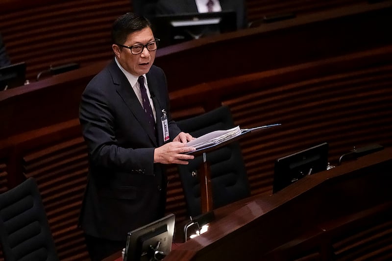 Chris Tang, wearing a dark suit, red tie and glasses, reads from a stack of paper on a podium.