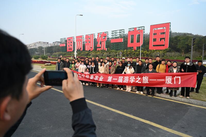 2024年1月12日，福建厦门竖起一个台湾金门岛可见的“一国两制统一中国”标语牌，游客在拍照。