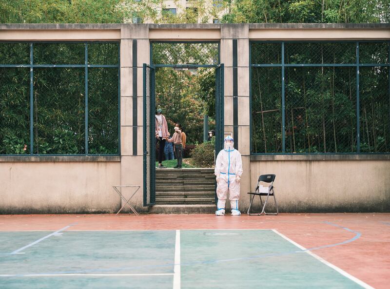 A community volunteer wearing personal protective equipment stands as residents line up during a test for the Covid-19 coronavirus in a compound during a Covid-19 lockdown in Pudong district in Shanghai on April 19, 2022. Credit: AFP.