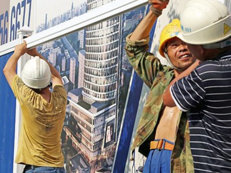 Chinese migrant workers build partition walls in front of a billboard at the construction site of a residential property project in Shanghai, Aug. 24, 2016. 