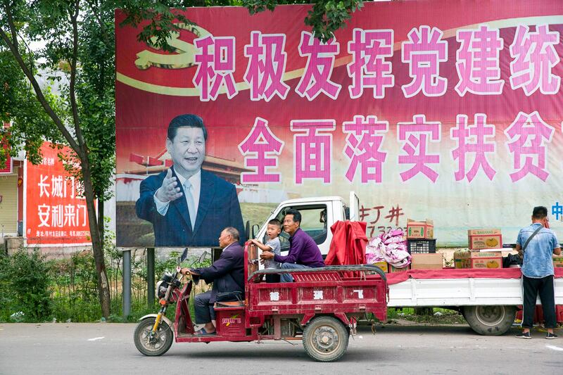 Residents pass by a poster of Chinese President Xi Jinping and slogans which read "Actively play the leading role of party building and comprehensively implement the plan for poverty alleviation" near Pingdingshan city in central China's Henan province, June 2, 2018. (Ng Han Guan/AP)