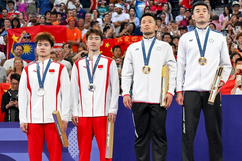 Taiwan's gold medalists (R) Lee Yang and Wang Chi-lin and China's silver medalists Liang Weikeng and Wang Chang stand up for the anthem of Chinese Taipei on the podium at the men's doubles badminton medal ceremony during the Paris 2024 Olympic Games at Porte de la Chapelle Arena in Paris, Aug. 4, 2024. (Arun Sankar/AFP)