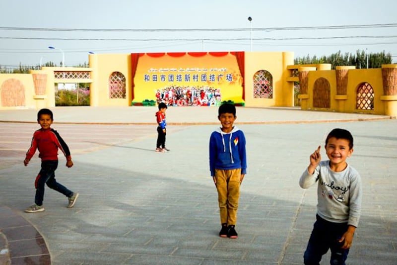 Uyghur children play in a square where a propaganda poster shows Han Chinese and Uyghurs posing together in a photograph with the words 'Hotan City Unity New Village Unity Square' at the Unity New Village in Hotan, northwestern China's Xinjiang region, Sept. 20, 2018. (Andy Wong/AP)