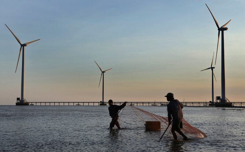 Men use a net to catch fish in the foreground of wind turbines along the southern coastal province of Bac Lieu in 2014. Danish renewable energy giant Ørsted announced that it was leaving Vietnam's wind market in June 2023, stating that “Our business ethics have met hurdles.” (Duy Khoi/AFP)