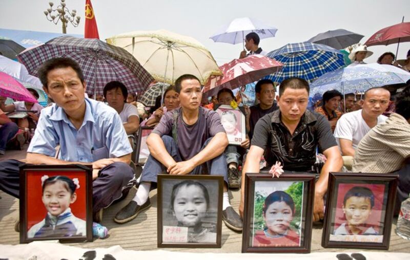 Fathers sit in front of photos of their children during a quiet protest outside the government office in Mianzhu in southwestern China's Sichuan province, June 1, 2008. (Nir Elias/Reuters)