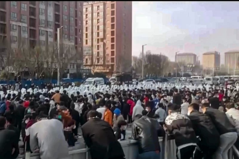 Protesters face off against security personnel in white protective clothing at the factory compound operated by Foxconn Technology Group in Zhengzhou in central China's Henan province, Nov. 23, 2022. Credit: AP