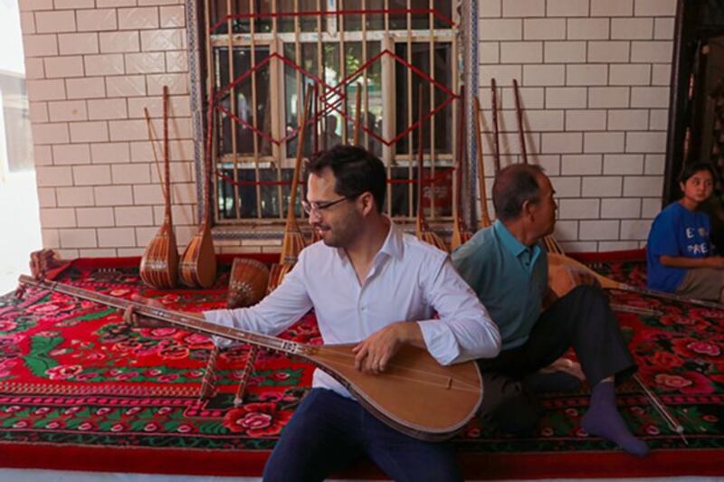 Hector Dorbecker, counselor for economic-commercial and financial affairs at the Embassy of Mexico in Beijing, tries to play dutar, a long-necked two-stringed lute, in Jiayi village of Xinhe county in northwestern China's Xinjiang region, Aug. 2, 2023. (Zhao Chenjie/Xinhua via Getty Images)