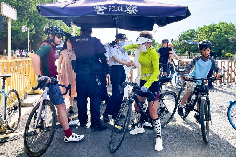 A foreigner waits on his bicycle as people on bicycles are ordered to stop for identification check at a checkpoint along a street near Tiananmen Square in Beijing, June 4, 2023. (Andy Wong/AP)