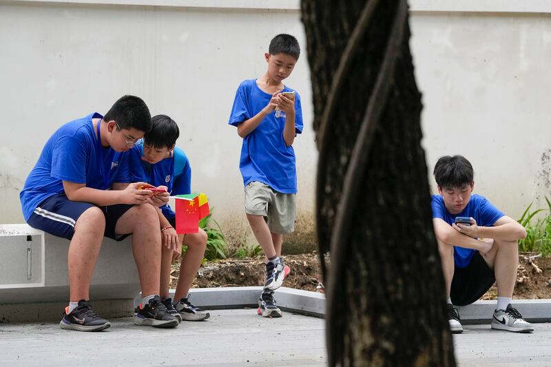 Youths look at their smartphones on the street in Beijing, Thursday, Aug. 3, 2023. (Ng Han Guan/AP)