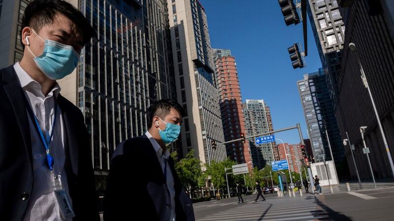 People wearing face masks amid the concerns over the COVID-19 coronavirus walk on a nearly empty street in the Chinese capital Beijing, April 23, 2020. 