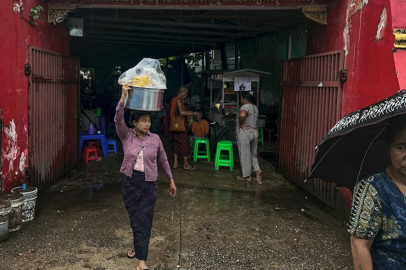 A street food vendor carries a pot on her head during a rain shower in Yangon, June 18, 2024. (Sai Aung Main/AFP)