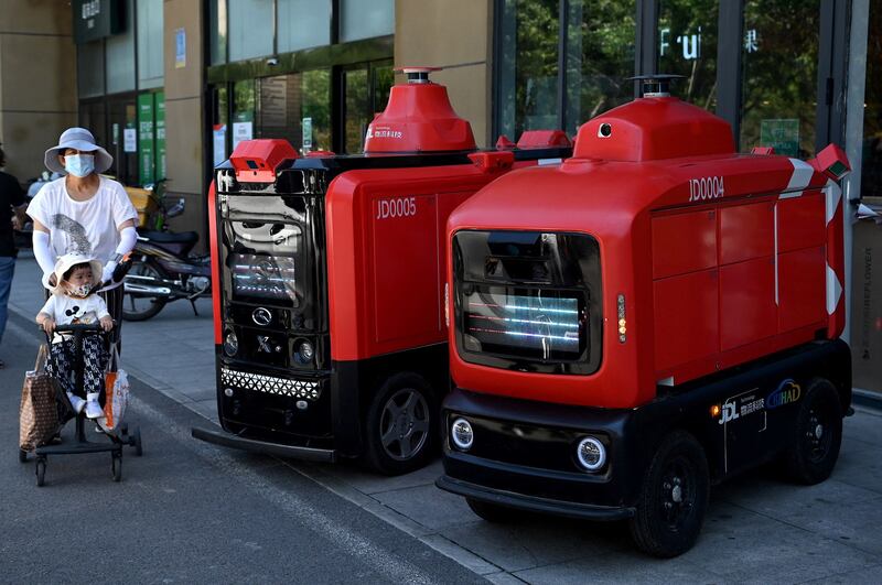 People walk past Chinese e-commerce giant JD.com's autonomous vehicles used to deliver goods to customers, outside a supermarket in Beijing, June 18, 2021. Credit: AFP