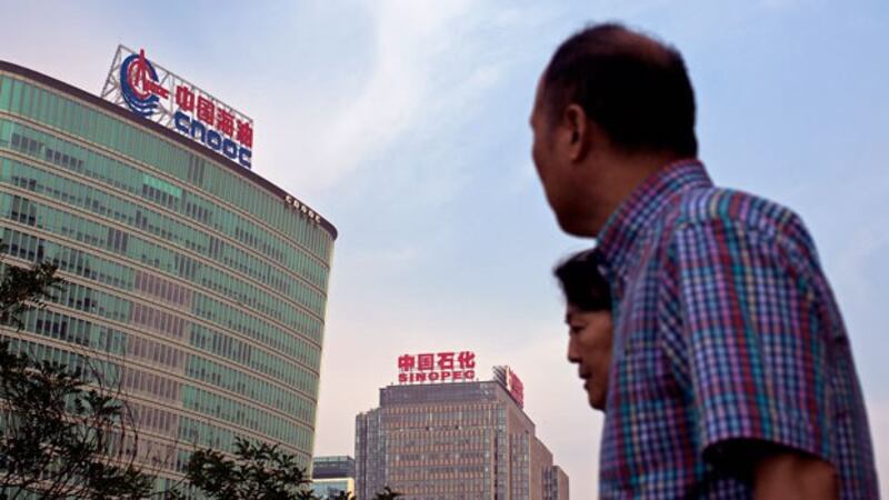 People walk past the headquarters of China National Offshore Oil Corp. (L) and China Petroleum & Chemical Corp. (Sinopec) (C) in Beijing, Sept. 14, 2015.