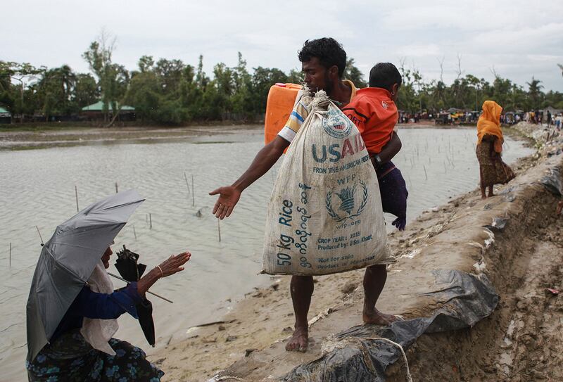 A Rohingya refugee carrying a USAID bag reaches out to a woman as they arrive in Teknaf, Bangladesh on Sept. 9, 2017, after fleeing violence in neighboring Myanmar.