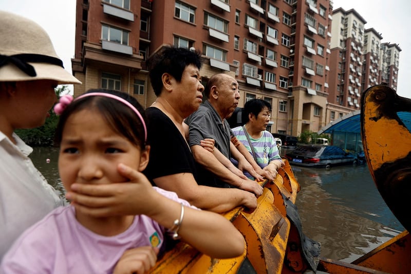 People stand on a front loader as they're evacuated from a flooded residential compound after flooding brought by remnants of Typhoon Doksuri, in Zhuozhou, Hebei province, China, Aug. 3, 2023. Credit: Tingshu Wang/Reuters