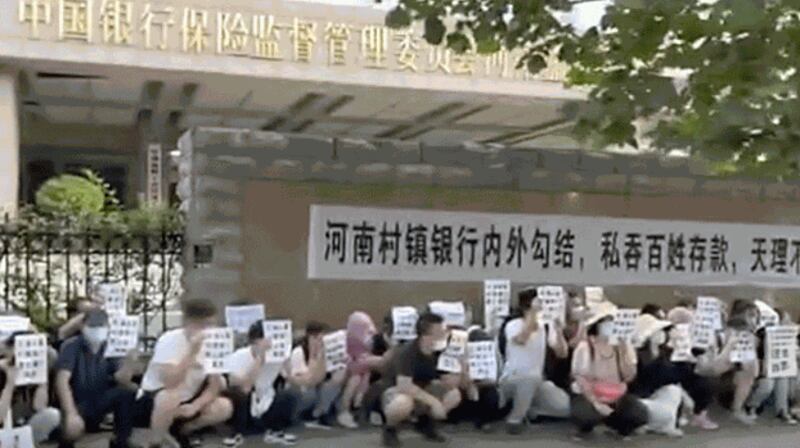 Demonstrators hold banners during a protest over the freezing of deposits by rural-based banks, outside a People's Bank of China building in Zhengzhou, capital of central China's Henan province, July 10, 2022. Credit: Screengrab via Reuters