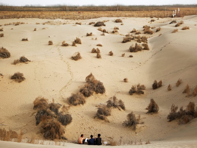 Men sit at the foot of a dune in Taklamakan Desert, Hotan, Xinjiang Uighur Autonomous Region, China, March 21, 2017.