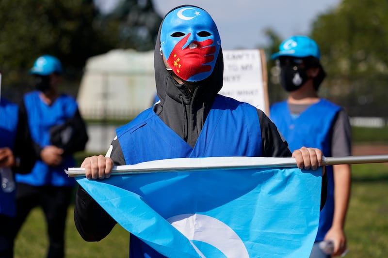 A man wears a mask to protect members of his family who he says have been put into forced labor camps in China, as members of the Uyghur American Association rally in front of the White House, Oct. 1, 2020.