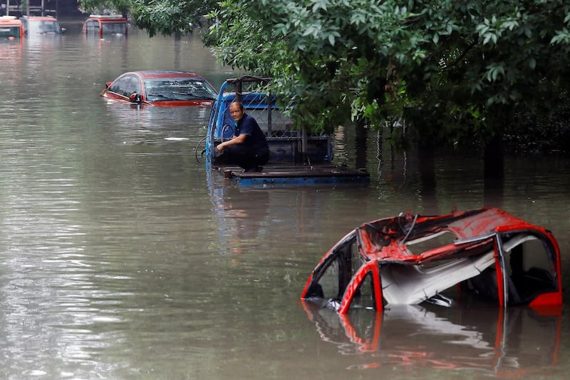 A man sits on a partially submerged vehicle in Zhuozhou, Hebei province, China, Aug. 3, 2023. Credit: Tingshu Wang/Reuters