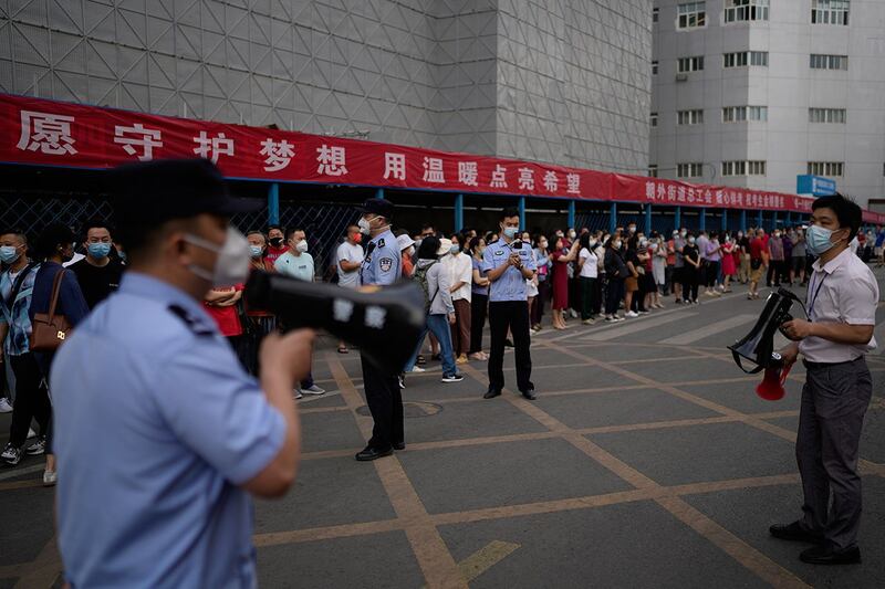 2022 年 6 月 7 日，在北京举行的中国全国高考第一天，警察，学校官员与学生家长在学校外。（美联社）