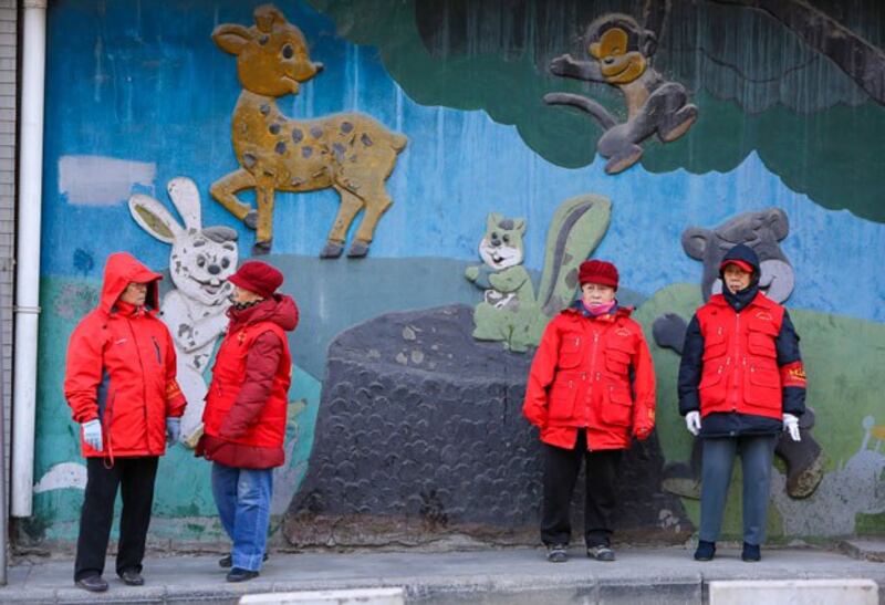 Elderly residents with red armbands, identifying them as security volunteers, stand on duty beside a road in central Beijing, Dec. 12, 2013. (Jason Lee/Reuters)