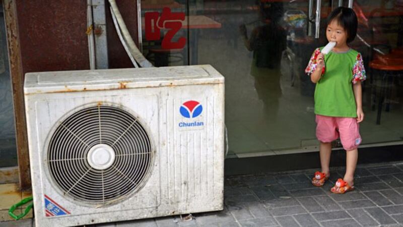 A young girl eats an popsicle while standing next to an air conditioning unit during a heat wave in Shanghai, China, in a file photo.